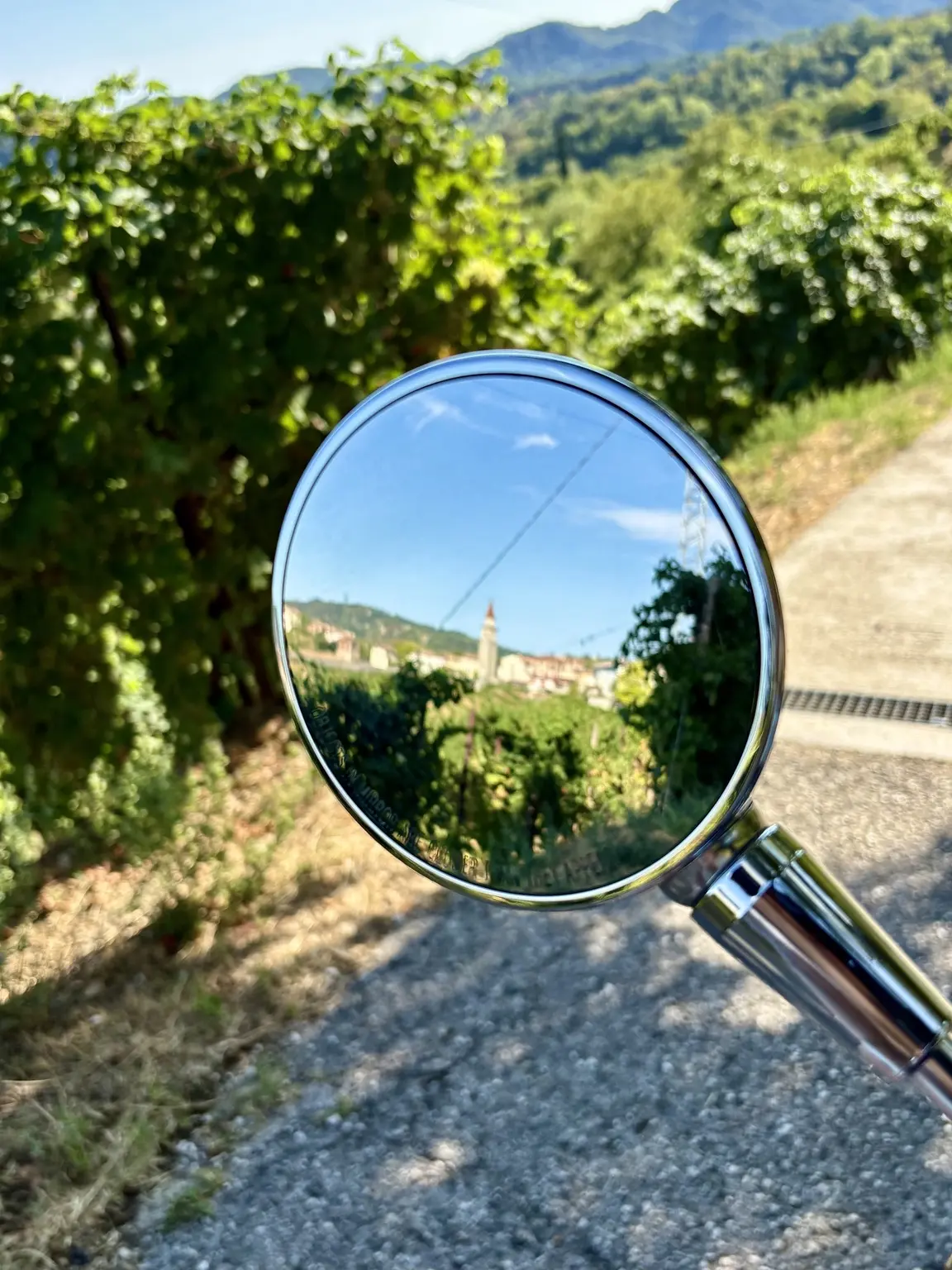 Vespa mirror reflecting a village and bell tower among the vineyards