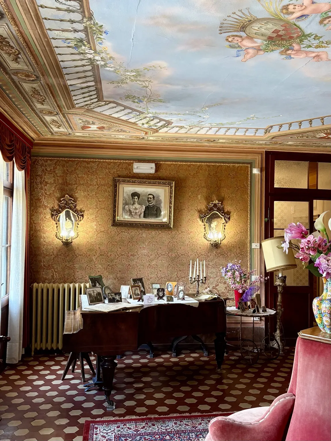 Salon at Villa Panigai with piano, photographs and decorated ceiling
